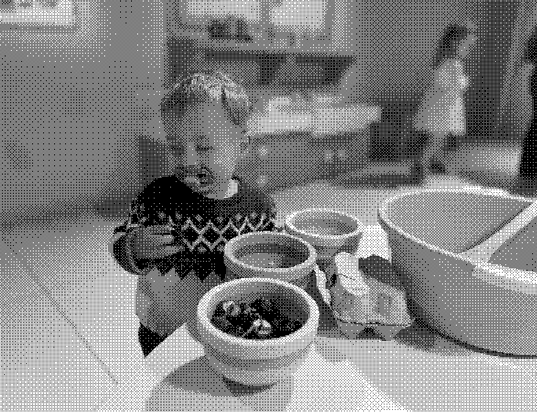 Toddler in a patterned sweater with a pacifier, surrounded by toy bowls of strawberries and a blue mixing bowl in a play kitchen.
